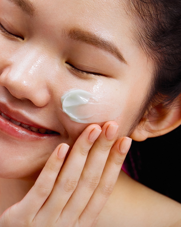 Woman smiles with dollops of Cicapair Gel moisturizer cream smoothed across her cheek.