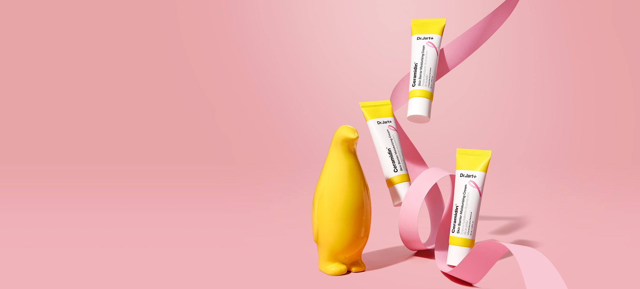 Penguin and artistically displayed pink breast cancer awareness ribbons among tube of ceramidin cream.